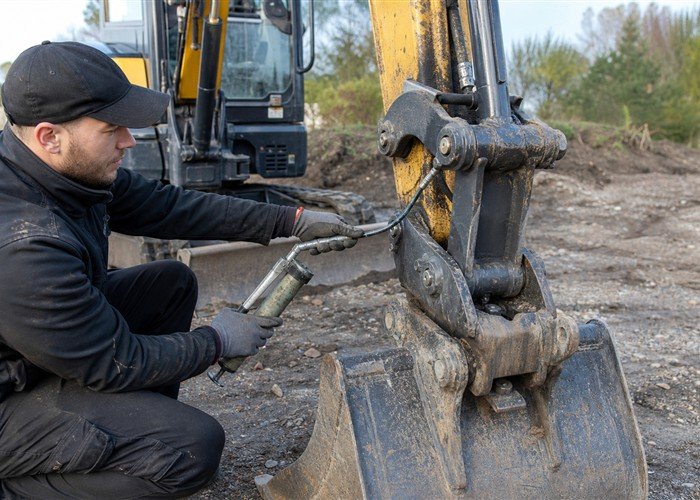 Technician greasing mini excavator boom bucket pins and quick coupler during early service Technician greasing mini excavator boom bucket pins and quick coupler during early service