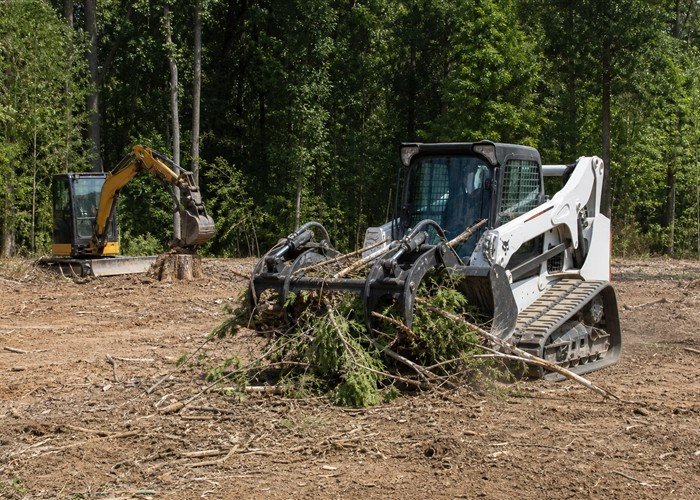 Skid steer with grapple moving brush while a mini excavator removes a stump Skid steer with grapple moving brush while a mini excavator removes a stump