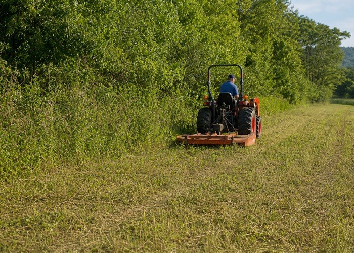Compact tractor with rotary cutter maintaining regrowth along a cleared field edge Compact tractor with rotary cutter maintaining regrowth along a cleared field edge