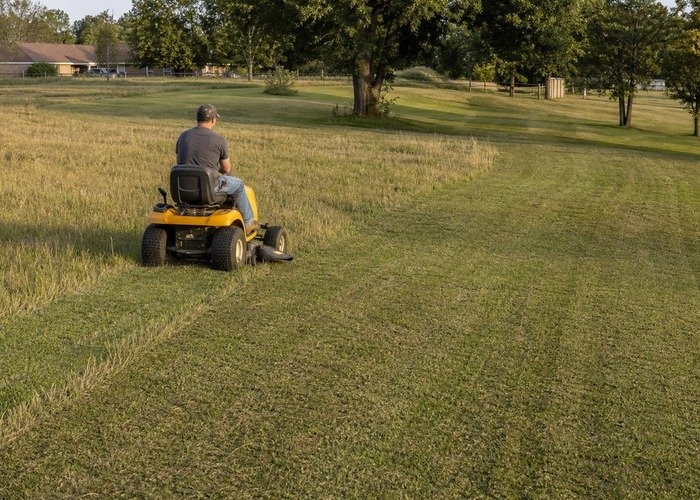 Riding mower making a slower second pass through tall mixed grass on an uneven rural lawn Riding mower making a slower second pass through tall mixed grass on an uneven rural lawn