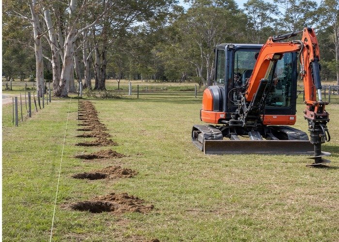 Mini excavator parked near a straight row of completed fence post holes Mini excavator parked near a straight row of completed fence post holes