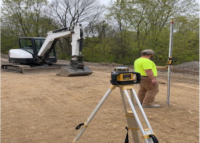 Operator checking a benchmark and grade rod beside a stopped excavator Operator checking a benchmark and grade rod beside a stopped excavator