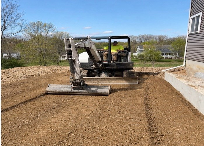 Mini excavator making a final grading pass away from a foundation Mini excavator making a final grading pass away from a foundation