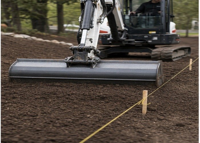 Smooth grading bucket back-dragging soil beside string line and grade stakes