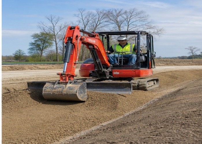 Mini excavator finishing a smooth drainage grade with a wide bucket