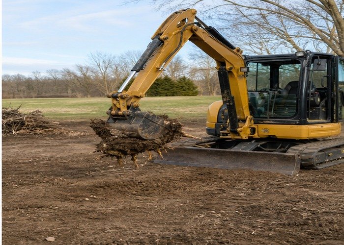 Mini excavator moving a loosened small stump low within a clear work zone Mini excavator moving a loosened small stump low within a clear work zone