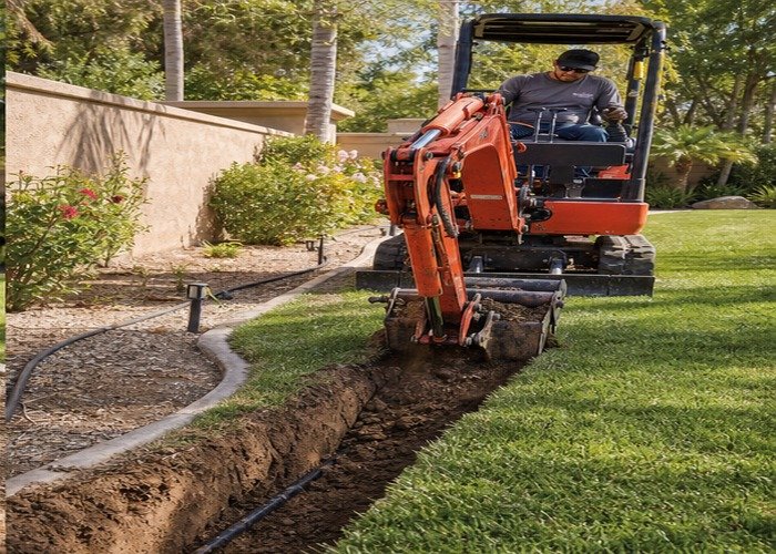 Mini excavator backfilling a narrow irrigation trench in a landscaped yard Mini excavator backfilling a narrow irrigation trench in a landscaped yard