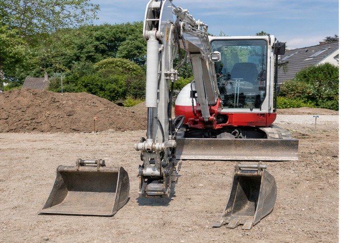 Mini excavator parked on level ground beside two buckets before an attachment change