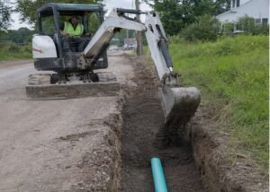 Mini excavator placing suitable backfill into a utility trench in shallow lifts