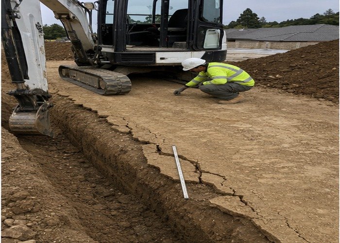 Operator inspecting track support and cracks beside a stopped mini excavator