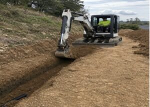 Mini excavator digging from a firm level working platform beside a trench