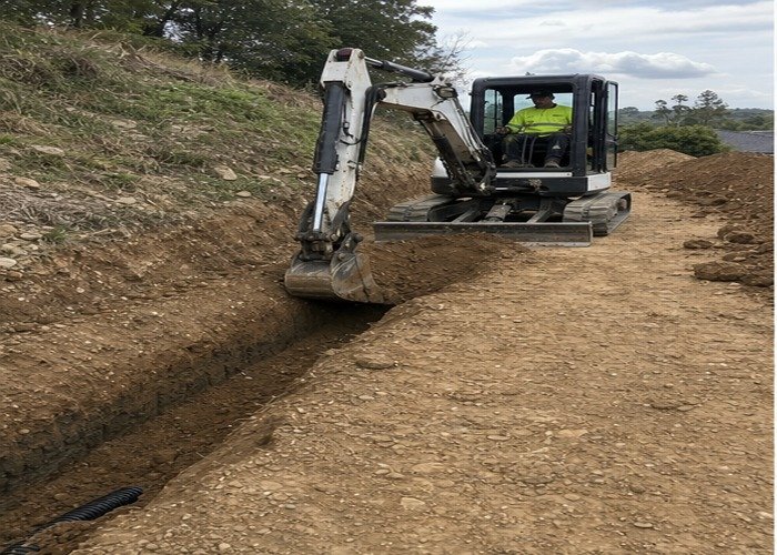 Mini excavator digging from a firm level working platform beside a trench