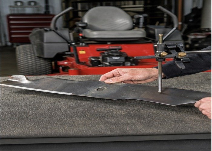 Removed mower blade being checked for edge condition and balance on a workbench