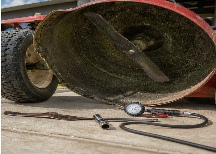 Safe mower deck underside inspection with blade and tire pressure tools visible Safe mower deck underside inspection with blade and tire pressure tools visible