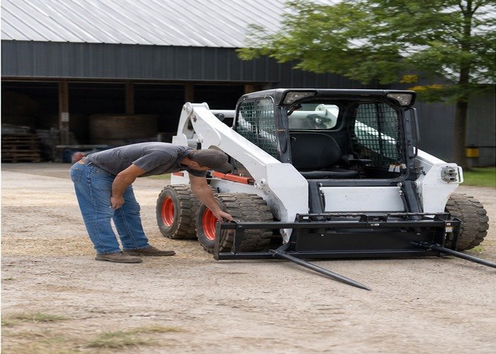 Operator inspecting grounded bale spear locks and tines Operator inspecting grounded bale spear locks and tines