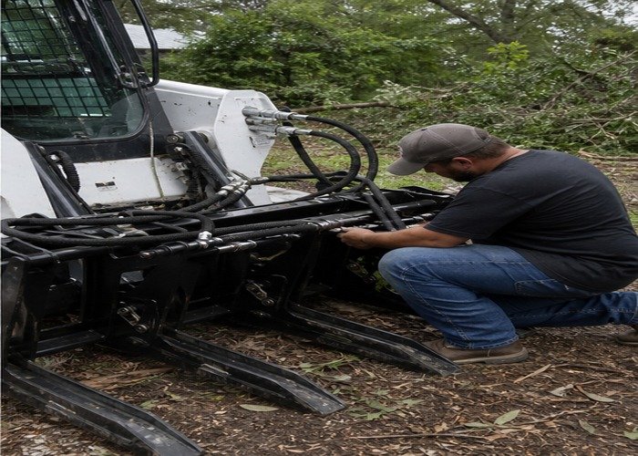 Operator inspecting skid steer grapple teeth hoses and couplers after brush work Operator inspecting skid steer grapple teeth hoses and couplers after brush work