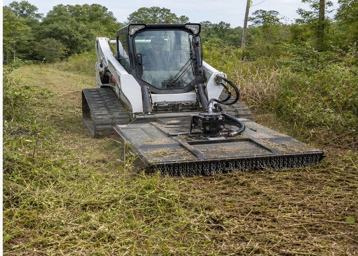 Skid steer brush cutter working in light vegetation with safe clearance Skid steer brush cutter working in light vegetation with safe clearance