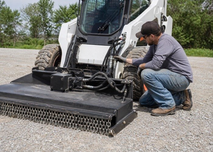 Skid steer auxiliary coupler inspection Operator inspecting skid steer auxiliary hydraulic couplers and hose routing before attachment use