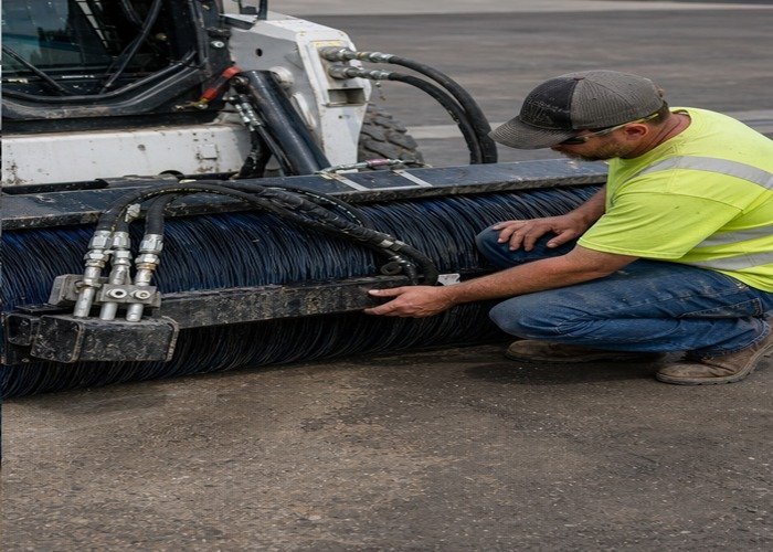 Operator inspecting rotary broom bristles hydraulic hoses and couplers after sweeping Operator inspecting rotary broom bristles hydraulic hoses and couplers after sweeping