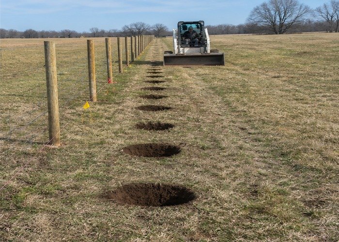 Row of clean evenly spaced post holes with a skid steer parked at the end Row of clean evenly spaced post holes with a skid steer parked at the end