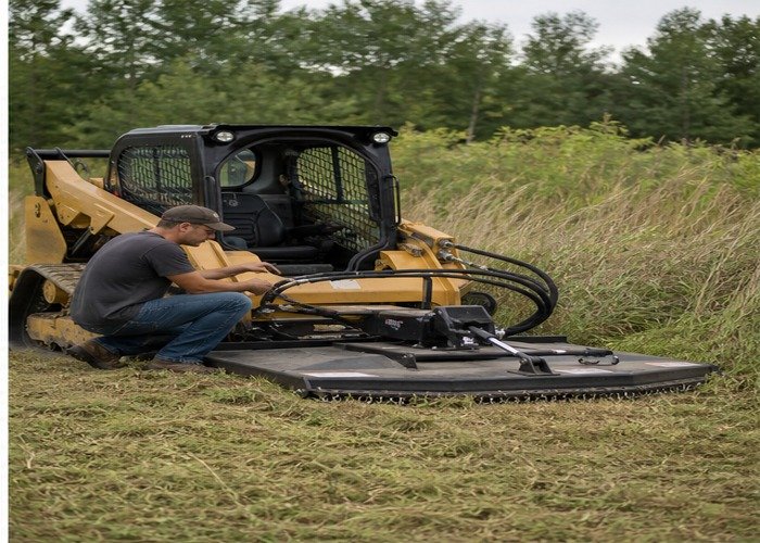 Operator inspecting guarded brush cutter deck and hydraulic hoses on a stopped skid steer Operator inspecting guarded brush cutter deck and hydraulic hoses on a stopped skid steer