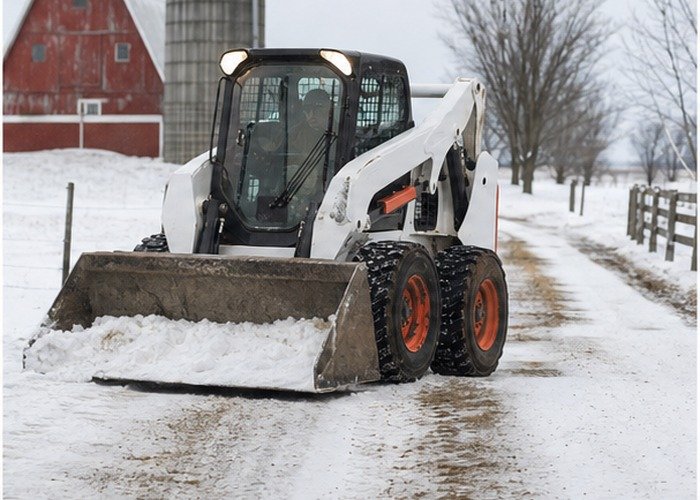 Skid steer bucket clearing snow from a farm lane with visible tire traction Skid steer bucket clearing snow from a farm lane with visible tire traction