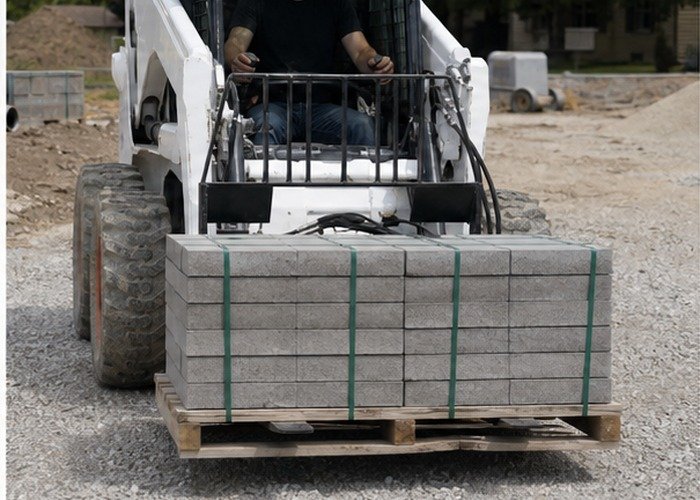 Skid steer carrying a pallet low across a gravel surface Skid steer carrying a pallet low across a gravel surface