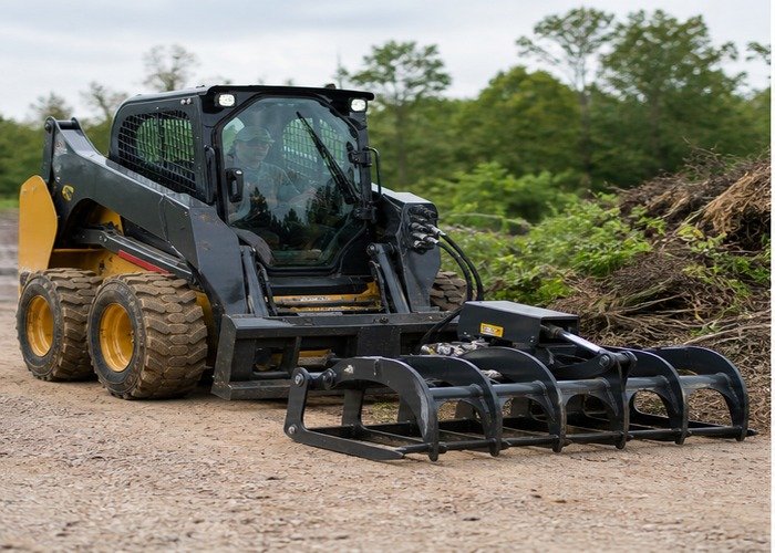 Enclosed-cab skid steer aligned with a grapple attachment on level ground