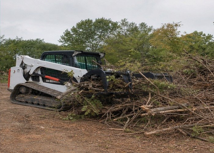 Skid steer sorting branches into an organized brush pile