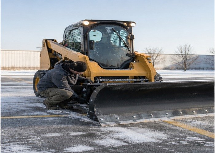Operator checking grounded snow pusher locks and cutting edge Operator checking grounded snow pusher locks and cutting edge