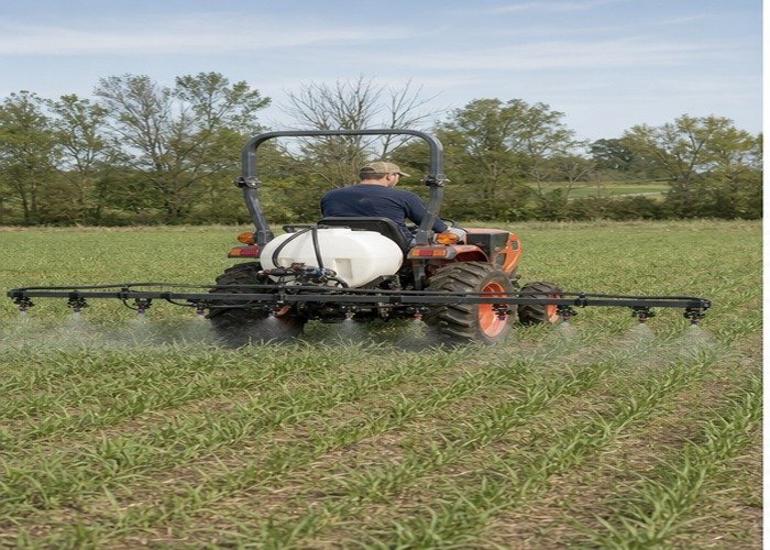 Compact tractor applying an even clean-water spray pattern with a rear boom