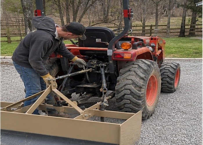Operator checking box blade scarifier depth and top-link adjustment on a stopped tractor Operator checking box blade scarifier depth and top-link adjustment on a stopped tractor