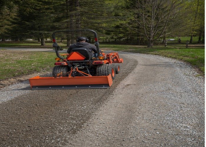 Compact tractor pulling a box blade to restore crown on a gravel driveway