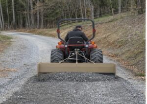 Compact tractor using a box blade to repair a gravel driveway crown