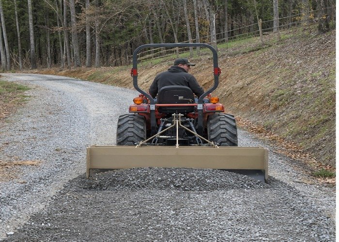Compact tractor using a box blade to repair a gravel driveway crown