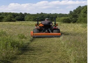 Compact tractor cutting tall mixed grass with a rear flail mower