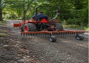 Compact tractor using a rear landscape rake to recover loose gravel on a rural lane