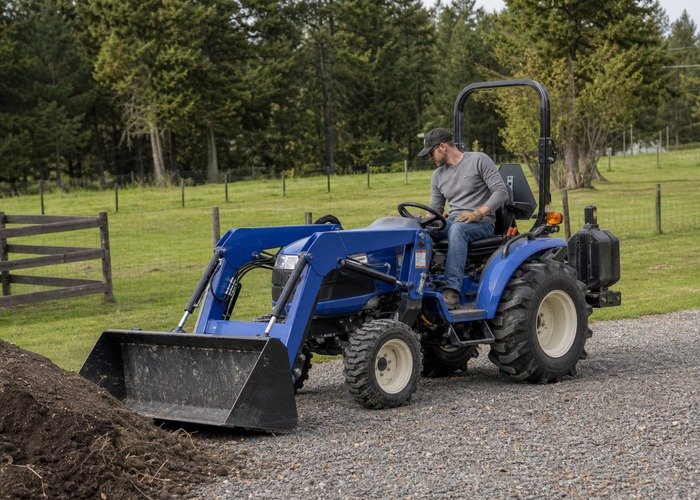 Operator checking compact tractor loader setup and rear ballast before moving soil
