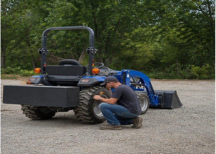 Operator inspecting rear ballast and tire condition on a stopped compact tractor Operator inspecting rear ballast and tire condition on a stopped compact tractor