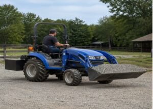 Compact tractor carrying gravel low with a rear ballast box on a level rural lane