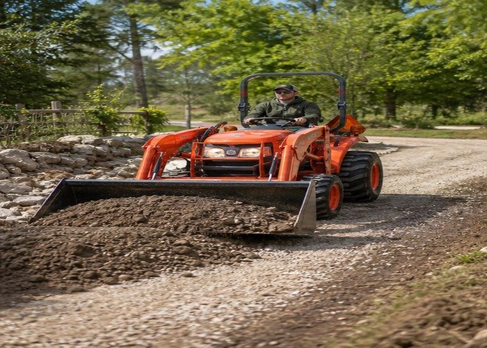 Compact tractor using a front loader to move gravel on a rural property lane Compact tractor using a front loader to move gravel on a rural property lane