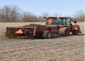 Compact tractor applying solid manure evenly across a dry field