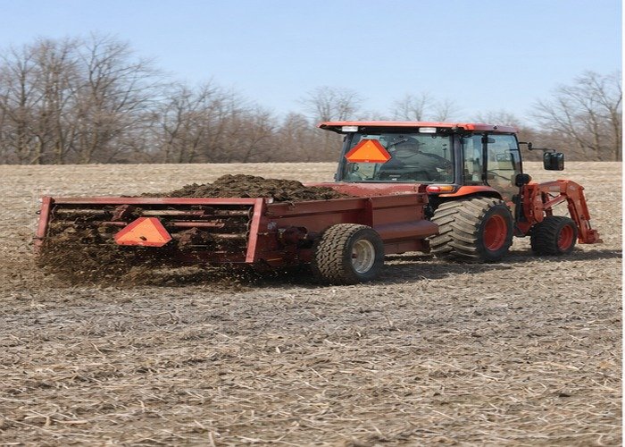 Compact tractor applying solid manure evenly across a dry field