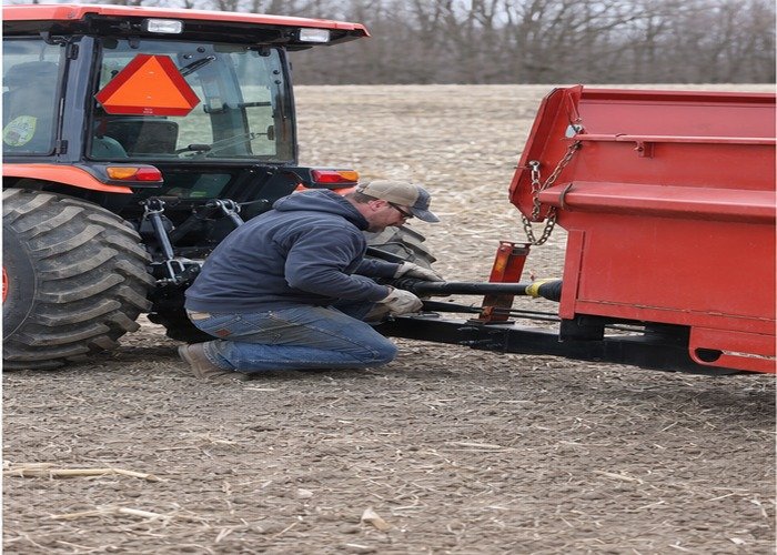 Operator checking a stopped manure spreader hitch and guarded PTO connection