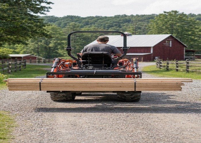 Compact tractor carrying a lumber bundle low and stable along a farm lane Compact tractor carrying a lumber bundle low and stable along a farm lane