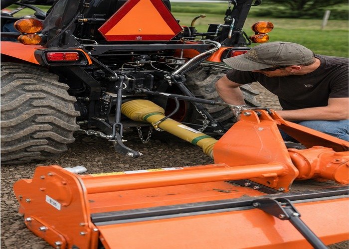 Operator checking guarded PTO shaft alignment on a stopped compact tractor