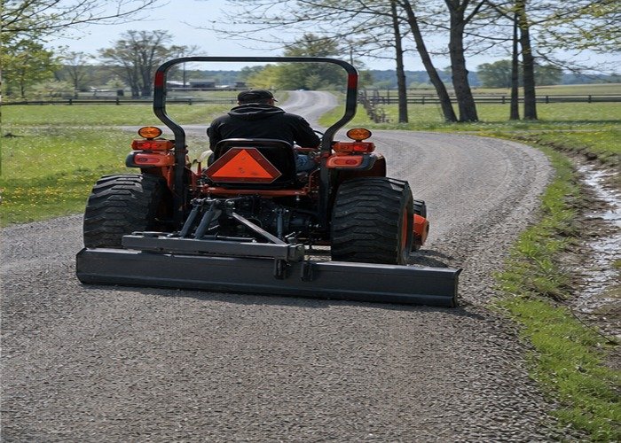 Compact tractor finishing a smooth crowned gravel lane with visible drainage edge
