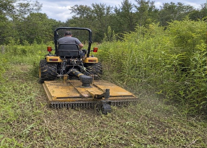 Compact tractor using a rotary cutter to mow tall brush at a rural field edge