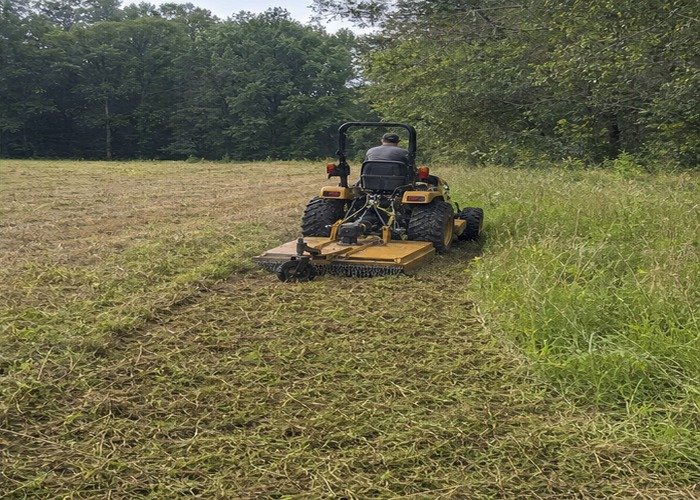 Compact tractor finishing a clean field edge after rotary cutting tall grass