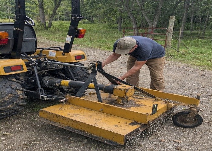 Operator checking PTO shield top link tailwheel and cutter height on a compact tractor